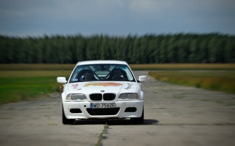 Białe BMW z zapalonymi światłami