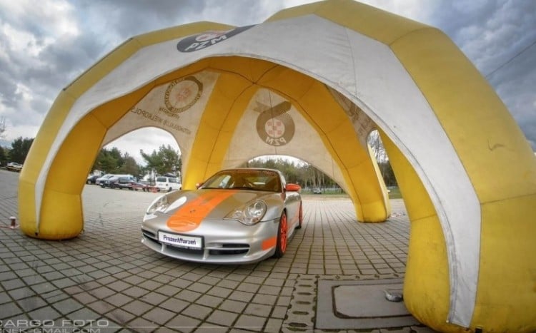 Na pierwszym planie srebrno-pomarańczowe Porsche, dalej białe auto