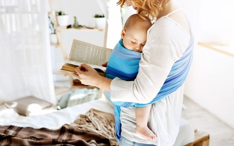 kobieta z dzieckiem w chuście czyta książkę