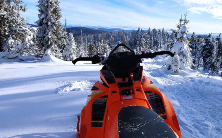 pomarańczowy skuter i widok na las oraz góry zimą