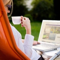 Kobieta korzystająca z laptopa trzymająca filiżankę kawy