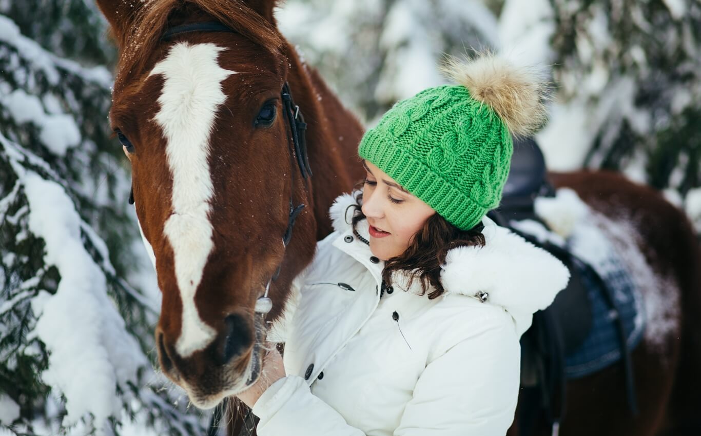 młoda kobieta głaszcze konia podczas zimowej jazdy po lesie