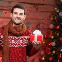 Mężczyzna trzymający prezent na tle choinki świątecznej