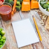 Notes z ołówkiem znajdujący się na drewnianym stole, wokół zdrowe jedzenie