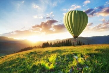 zielony balon na ogrzewane powietrze leci w górach na tle zachodu słońca