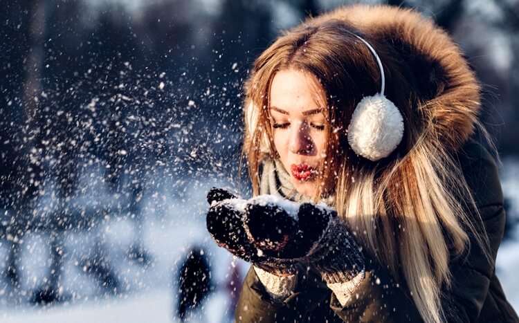 młoda kobieta zdmuchuje śnieg z wełnianych rękawiczek