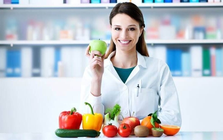 młoda kobieta dietetyk uśmiecha się w gabinecie trzymając w ręku jabłko