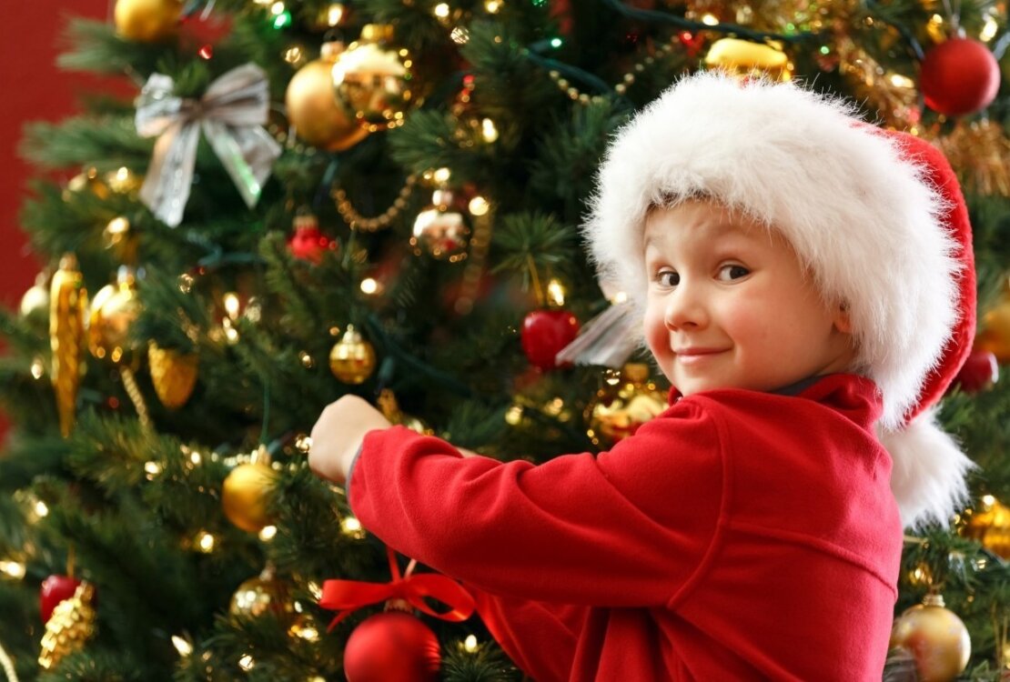 Dziecko w czapce Mikołaja ubierające choinkę