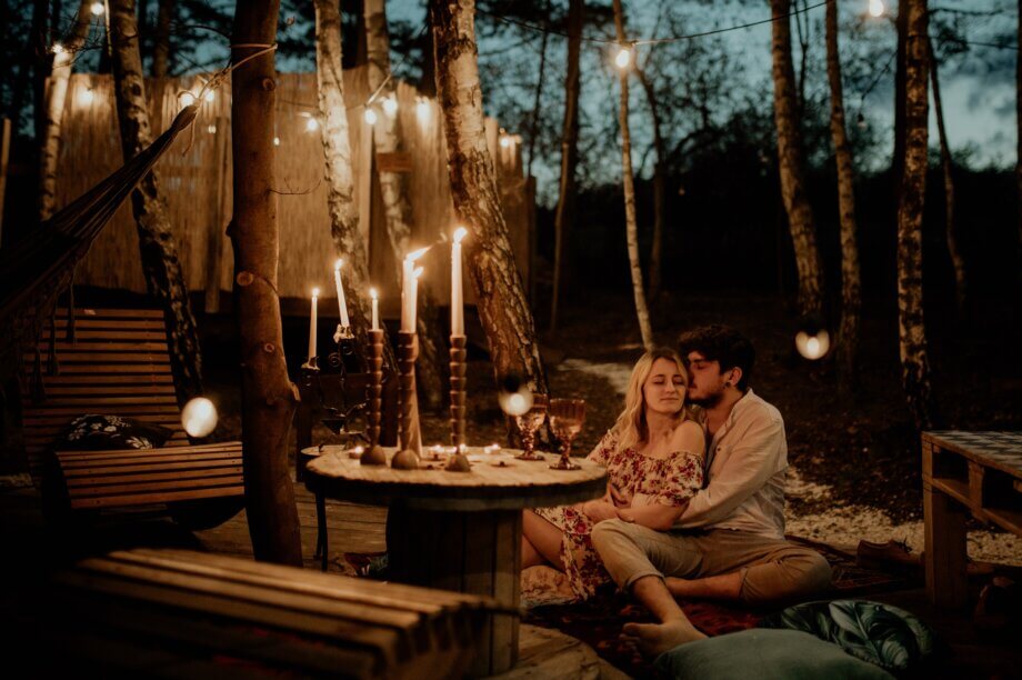 Para zakochanych siedząca w lesie przy zapalonych świecach.