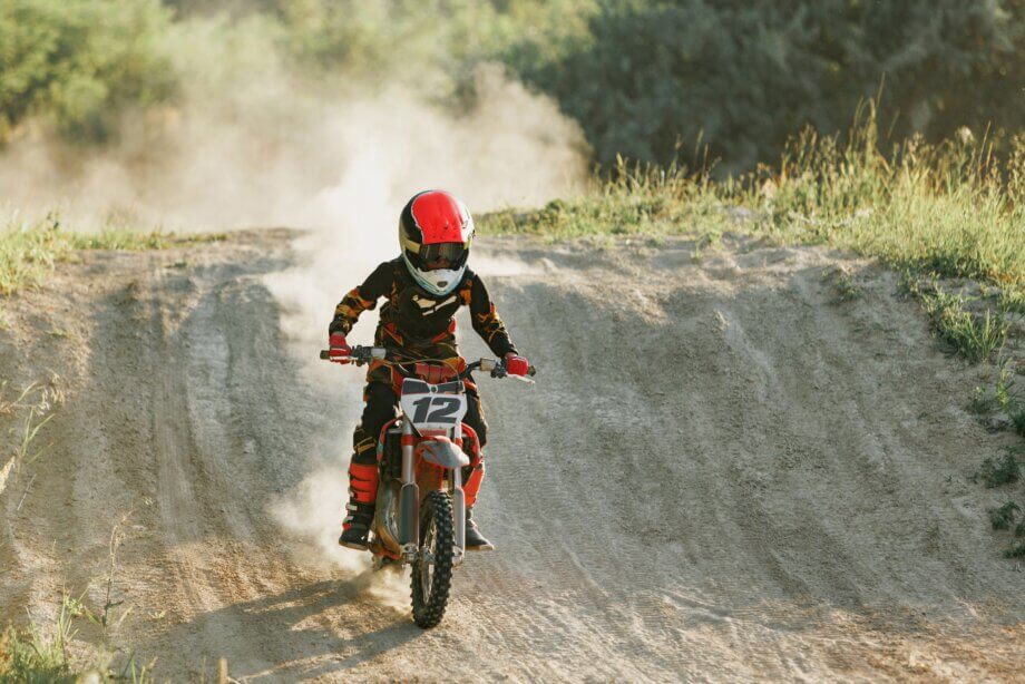 Chłopiec w kasku i pełnym ubraniu jadący z górki na motocrossie