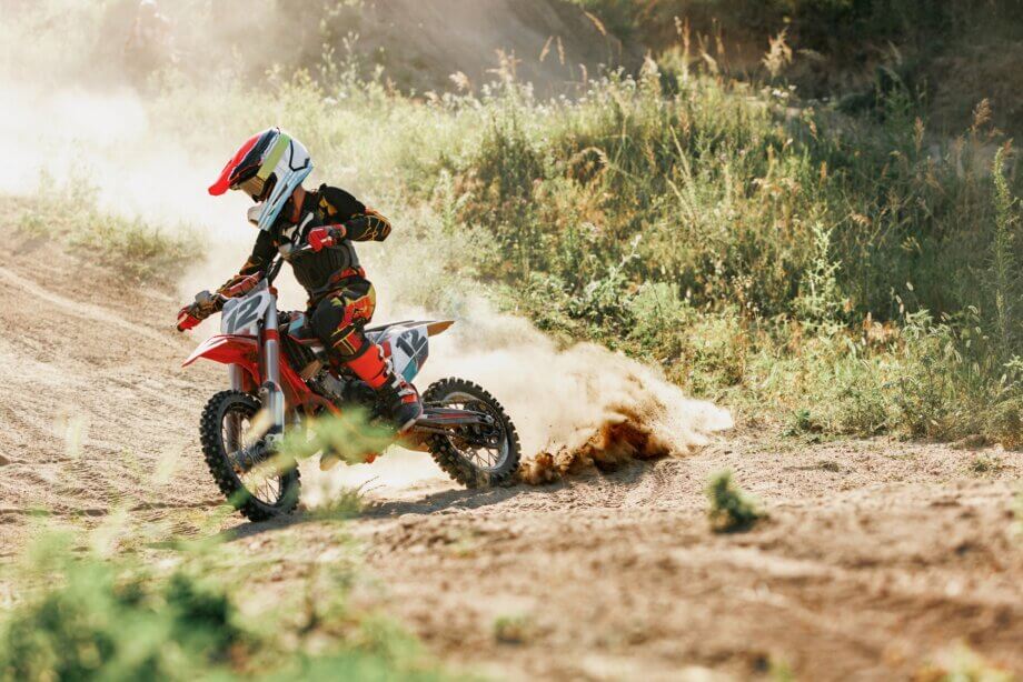 Chłopiec w kasku i pełnym ubraniu jadący na motocrossie i rozrzucający kołem piach