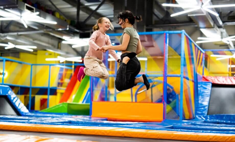 Dwie dziewczyny skaczące razem na kolorowej trampolinie w parku zabaw