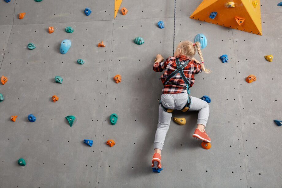 Dziewczynka w blond warkoczu wspinająca się po ściance wspinaczkowej