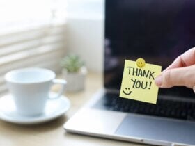 Dłoń trzymająca karteczkę z napisem "thank you" na tle laptopa