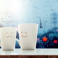 Dwa kubki z narysowanymi emocjami smutku i uśmiechu